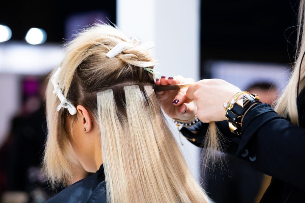 Professional Hairdresser Making Hair Extensions For Blonde Girl In A Beauty Salon